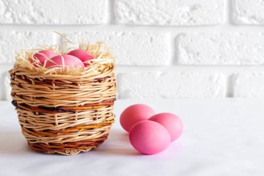 Hasır sepeti ve beyaz arka planda pembe renkli yumurtaları olan minimalist Paskalya kompozisyonu. Boşluğu kopyala