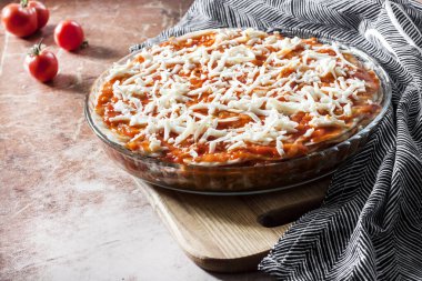 Ev yapımı lazanya ahşap tahtadaki yuvarlak cam fırın tabağında pişirmeye hazır.