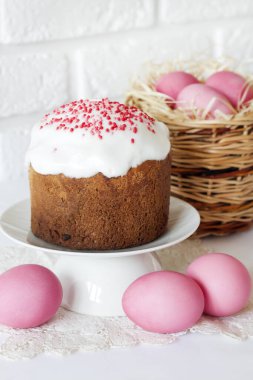Hasır sepetli, pembe yumurtalı ve beyaz arka planda Paskalya pastalı minimalist Paskalya kompozisyonu.