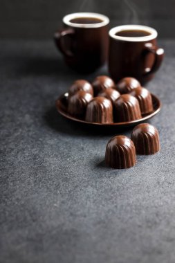 Bir tabakta çikolata şekeri ve iki fincan siyah arka planda fotokopi alanı olan sıcak kahve.