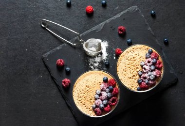 Ryazhenka (mayalanmış pişmiş süt) taze böğürtlenlerle süslenmiş cam kaselerde krema. Düz konum, üst görünüm, kopyalama alanı 