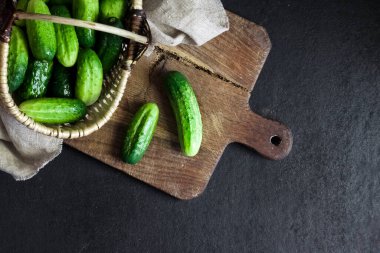 Hasır sepetteki taze salatalıklar tahtada, siyah arka planda..