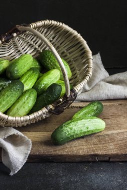 Hasır sepetteki taze salatalıklar tahtada, siyah arka planda..