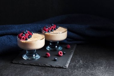 Ryazhenka (mayalanmış pişmiş süt) taze böğürtlenlerle süslenmiş cam kaselerde krema. 