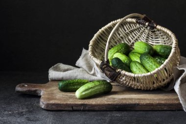 Hasır sepetteki taze salatalıklar tahtada, siyah arka planda..