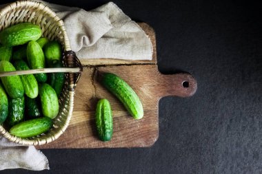 Hasır sepetteki taze salatalıklar tahtada, siyah arka planda..