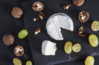 Brie peyniri. Üzümlü yumuşak peynir ve siyah arka planda ceviz. Düz yatış, üst görünüm