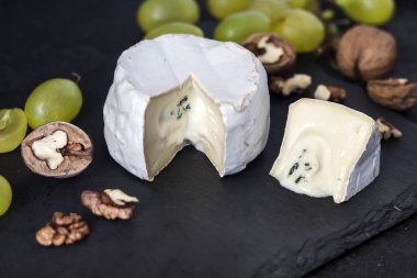 Brie peyniri. Üzümlü yumuşak peynir ve siyah arka planda ceviz.