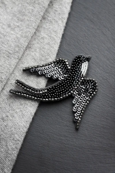 Seed bead embroidered brooch in a shape of black swallow bird on gray and black background