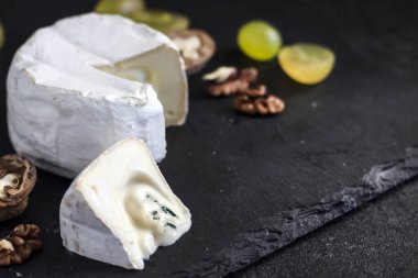 Brie peyniri. Üzümlü yumuşak peynir ve siyah arka planda ceviz. Boşluğu kopyala