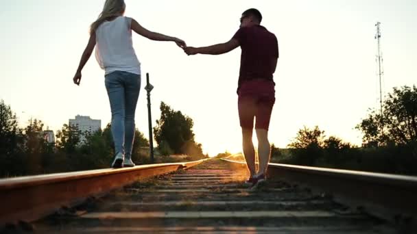 Boy and girl go on rails to the sunset. They hold each other's hand. — Stock Video