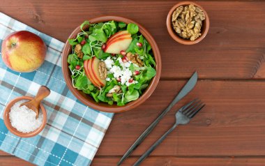 Elma dilimli yeşil salata ceviz ve ahşap masada yoğurt sosu.