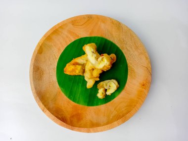 Kızarmış muz, beyaz arka planda izole edilmiş, ahşap bir tabakta servis edilen birkaç parçaya bölünmüş..