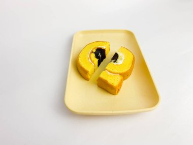 Rolltart moka with vanilla cream, halved, served on a square plate, isolated on white background.