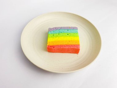 Rainbow slice cake served on a round plate, isolated on white background.