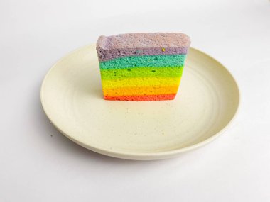 Rainbow slice cake served on a round plate, isolated on white background.