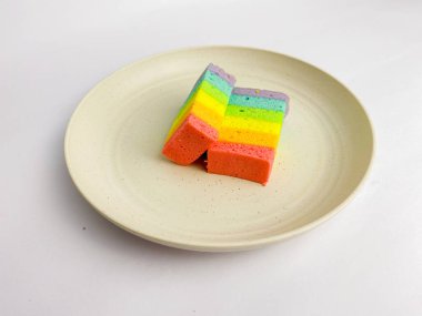 Rainbow slice cake cut in half, served on a round plate, isolated on a white background.