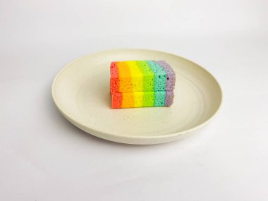 Rainbow slice cake cut in half, served on a round plate, isolated on a white background.