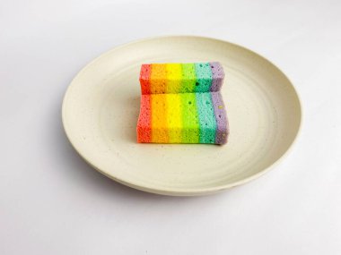 Rainbow slice cake cut in half, served on a round plate, isolated on a white background.