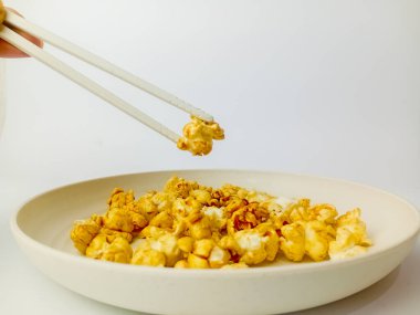 El, beyaz bir arka planda izole edilmiş yuvarlak tabakta çubuklarla tatlı karamelli patlamış mısır topluyor..