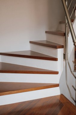 Beyaz duvarları, şık mimarisi ve rahat ev dekorasyonu olan kahverengi parke basamaklı sarmal merdiven..