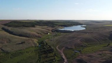 Ukrayna 'nın Maloyanisol köyü yakınlarındaki yuvarlanan tepeler ve tarlalarla çevrili kırsal bir rezervuar ve barajın panoramik drone görüntüsü. Yüksek kaliteli FullHD görüntüler