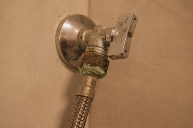 Makro, modası geçmiş ya da ihmal edilmiş bir tesisat tesisatının detaylarını çekmiş. Metal yüzey, sert su kaynaklı yeşil-mavi oksitlenme ve mineral tortuları ile görünür bir şekilde lekelenmiş. Tesisatı, bakım sorunlarını veya pas sorunlarını temsil eder