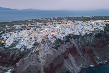 Yunanistan 'ın Santorini adasının ünlü uçurum kenarı mimarisinin Ege Denizi üzerinde parlayan ışıklarıyla gece karanlığı manzarası.