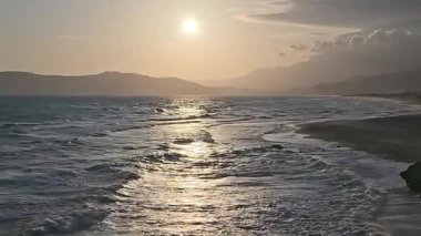 Akdeniz 'in altın saat manzarası Yunanistan' ın Girit kentindeki kumlu bir plaja çarpıyor. Gün batımında ya da gün doğumunda siluetli dağlarla sakin kıyı manzarası