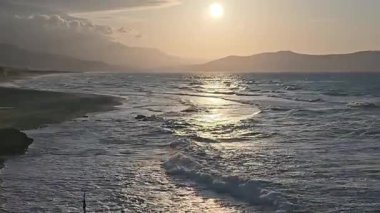 Akdeniz 'in altın saat manzarası Yunanistan' ın Girit kentindeki kumlu bir plaja çarpıyor. Gün batımında ya da gün doğumunda siluetli dağlarla sakin kıyı manzarası