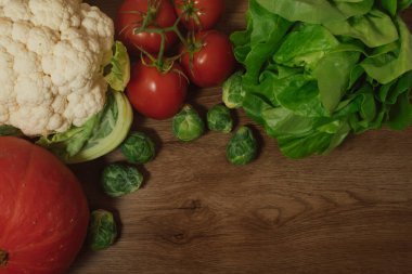 Yapraklı marul da dahil olmak üzere zengin bir organik ürün çeşitliliği, pazarlama metni için açık alanı olan ahşap bir arka planda yaratıcı bir şekilde düzenlenmiştir.