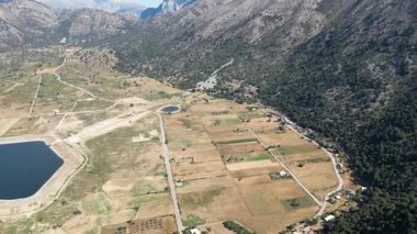 Omalos ovasının, dağların ve insan yapımı rezervuarın doğa ve altyapı manzarası. Doğal coğrafya ile mühendislik arasındaki zıtlık, su kullanımı ve geliştirme temaları için uygundur