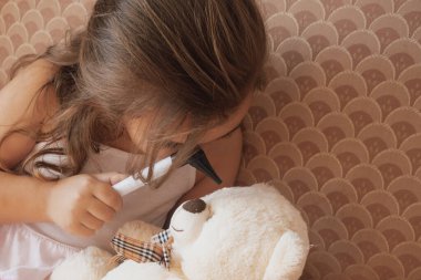 Yaratıcı oyun: kız pelüş oyuncağında tıbbi bir araç kullanıyor, hayal gücünü ve empatiyi teşvik ediyor. Bu yakın çekim erken gelişimi, rol yapma yoluyla öğrenmeyi ve bakım becerilerinin geliştirilmesini ön plana çıkarır.