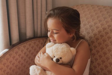 Gerçek mutluluk: gülümseyen bir kız oyuncak ayısını ezici bir sevgiyle kucaklar. Duygusal refah, olumlu aile anları ve erken yaşamın basit zevkleri için mükemmel bir tema.