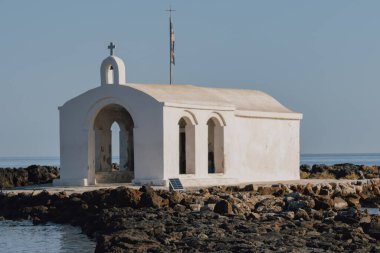 Georgioupolis Girit 'teki Aziz Nicholas kilisesinde gündüz manzaralı bir kompozisyon ile kayalık bir yürüyüş yolu ve çevreleyen su bulunuyor.
