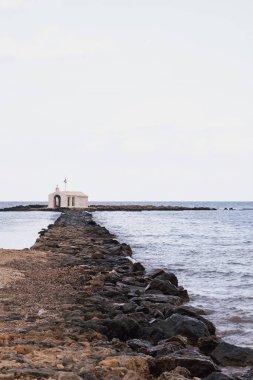 Georgioupolis Girit 'teki Aziz Nicholas kilisesinde gündüz manzaralı bir kompozisyon ile kayalık bir yürüyüş yolu ve çevreleyen su bulunuyor.