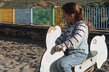 Playground fun: a child on a colourful spring toy in the shape of a bunny or rabbit. This shot is excellent for themes of kindergarten, school recess, and community park development