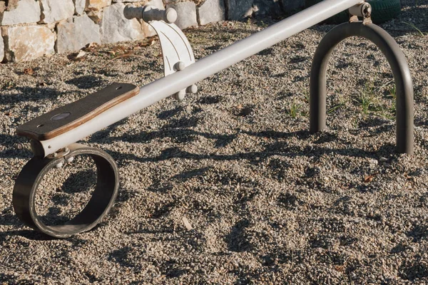 Boş bir oyun parkının yakın çekimi, metal ve ahşap bileşenlerine odaklanmış tahterevalli gibi. Görüntü, çocuklar için açık hava oyun ekipmanlarının inşaat, aşınma ve güvenlik özelliklerini vurguluyor