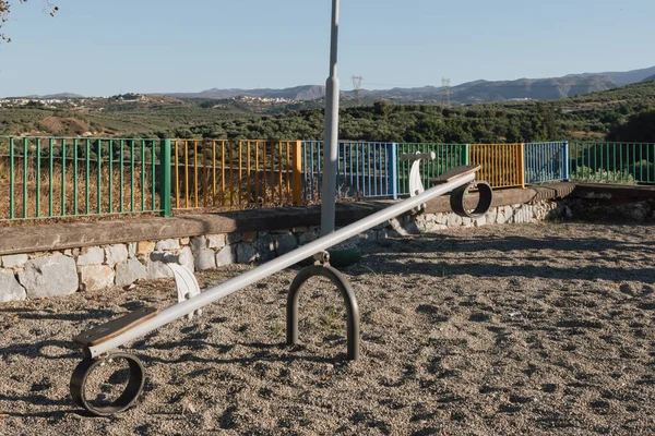 Oyun ekipmanları: Zeytin ağaçlarının desteklediği güneşli bir parkta yüz yüze salıncak. Bu sahne, resim gibi kırsal bir ortamda çocukluğun sakin anlarını ve beklentilerini hatırlatıyor.