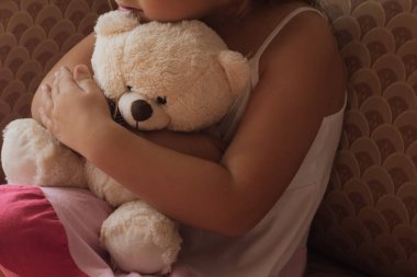 Küçük ellerin, yumuşak, sevilen bir oyuncak ayıyı sıkıca kavradığı yakın çekim. Bu görüntü, rahatlığın, güvenliğin sıcaklığını ve bir çocukla bir yoldaş arasındaki basit, derin duygusal bağı aktarır.