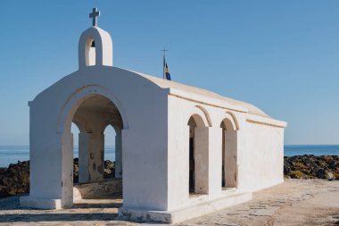 Georgioupolis Girit 'teki Aziz Nicholas kilisesinde gündüz manzaralı bir kompozisyon ile kayalık bir yürüyüş yolu ve çevreleyen su bulunuyor.