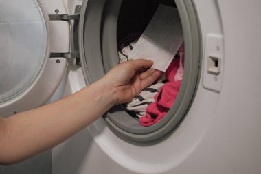 Çamaşır makinesindeki parlak renkli çamaşırlar: koruyucu çarşafla giysi kalitesini korumak. Rutin ev işlerini ve canlı kıyafet görünüşünü koruma ihtiyacını temsil ediyor..