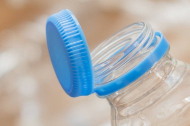 Mavi bir başlık berrak bir su şişesinin ağzında duruyor. Şişe, geri dönüşüm sorununu vurgulayan buruşmuş plastik atıklarla çevrili..
