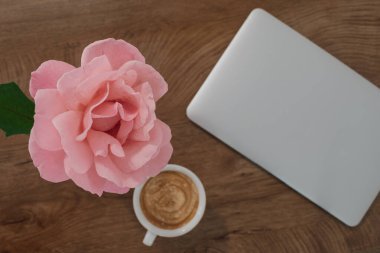 Düz kahve, pembe gül ve kapalı dizüstü bilgisayar: Sonbahar uzaktan kumandası için rahat atmosfer. Ev tabanlı yaratıcılık için rahat, sıcak ve ilham verici bir ortam yakalamak.