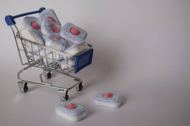 Metal bir sepette depolanmış bulaşık deterjanı kapsülleri ve tabletlerin yakın plan görüntüleri. Görüntü rengarenk temizlik ürünlerini ve yerli organizasyonu vurguluyor. Ev temizlik malzemeleri için ideal