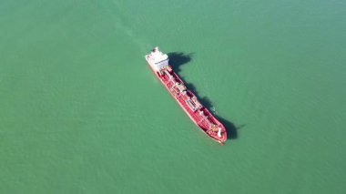 Zümrüt denizinde kırmızı gövdeli büyük bir kargo gemisine yakın çekim. 4K yatay dron görüntüsü, açık havada canlı yeşil suda yüzen kırmızı güverte ve cesetlerin detaylı görüntülerini yakalar..