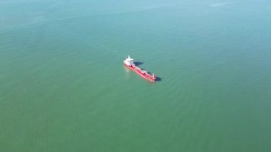 Zümrüt denizinde kırmızı gövdeli büyük bir kargo gemisine yakın çekim. 4K yatay dron görüntüsü, açık havada canlı yeşil suda yüzen kırmızı güverte ve cesetlerin detaylı görüntülerini yakalar..