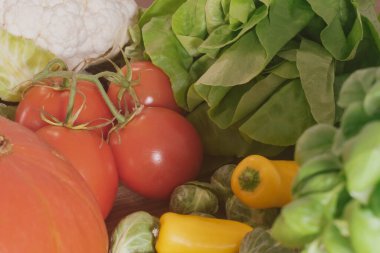 Domatesler ve yapraklı yeşillikler de dahil olmak üzere zengin bir ham, organik malzeme koleksiyonu, ahşap bir arka planda canlı bir mutfak kompozisyonu oluşturuyor.