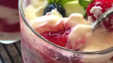 Camdan el kaşığı çilekli tiramisu. 4K yatay tatlı görüntüsü, sulu katmanlı, kremalı ve iştah açıcı görünümlü bir tatlı tatma anını gösteriyor..