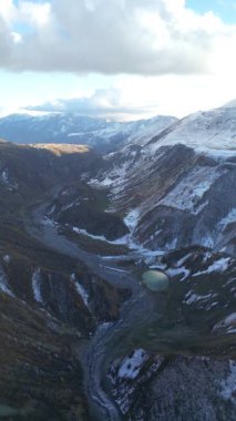 Kafkasya 'daki Alp Gölü' nün dikey kış manzarası. 4K seyahat insansız hava aracı görüntüleri, karla kaplı tepeleri ve açık gün ışığında sakin yüksek irtifa rezervuarı olan donmuş bir dağ manzarası gösteriyor..